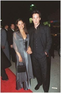 Jennifer syme and keanu reeves standing together wearing formal dresses and holding hands while smiling at the camera