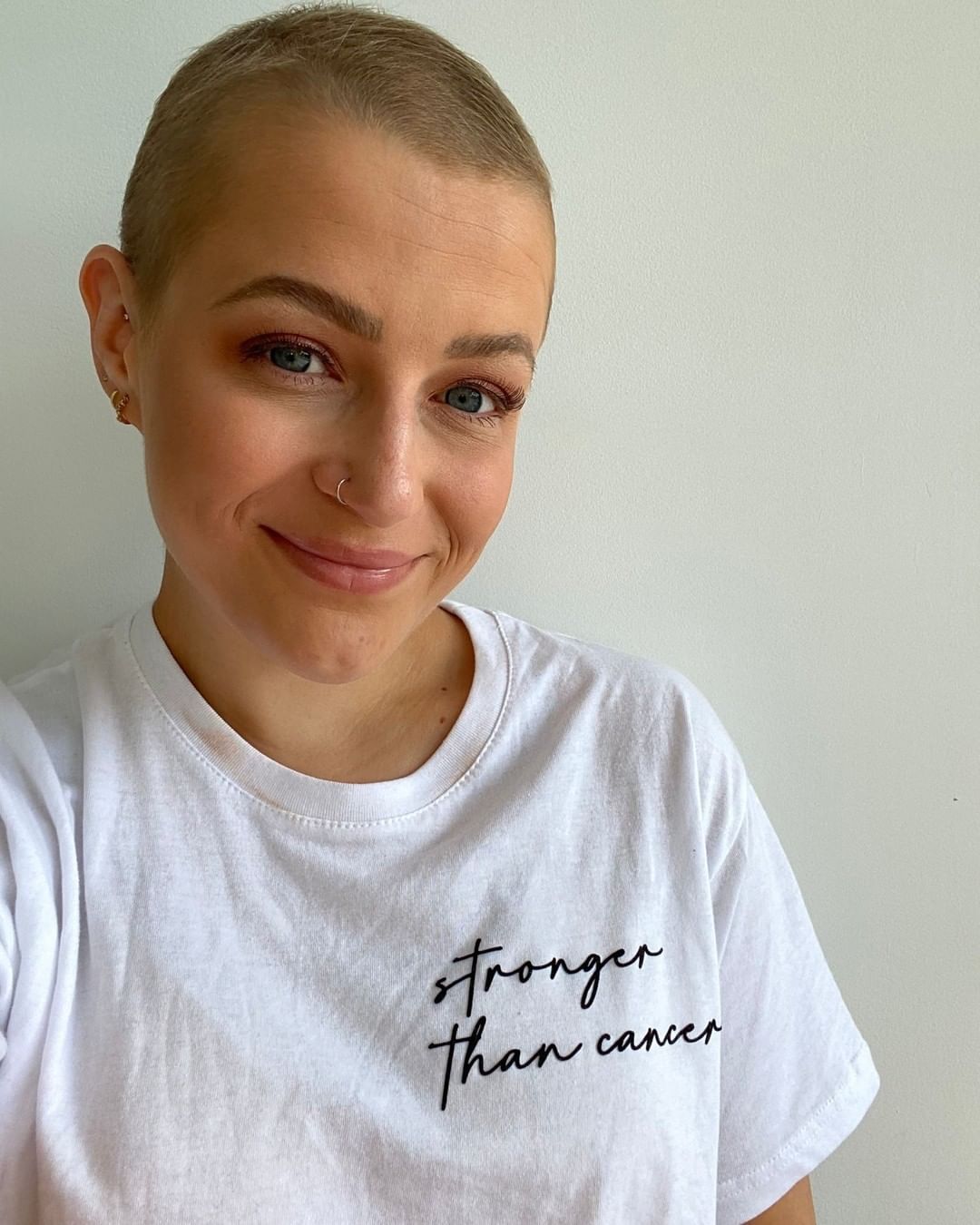 Smiling woman with breast cancer in white T-shirt, with the words ‘stronger than cancer’ in black cursive writing