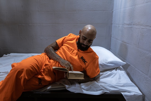 Bald tattooed male prisoner on his bed reading a thick book