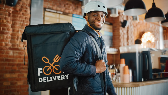 A food delivery rider wearing white helmet, jacket, and food case, inside a restaurant