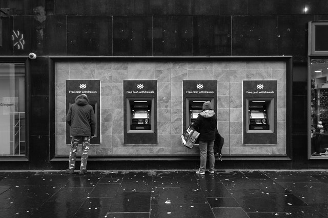 Four through-the-wall outdoor automated teller machines, with two people using the ATM