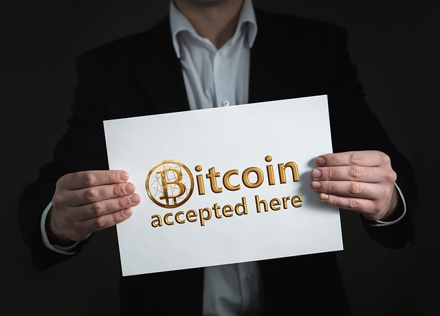 Man holding white paper with the words, ‘Bitcoin accepted here’ in gold