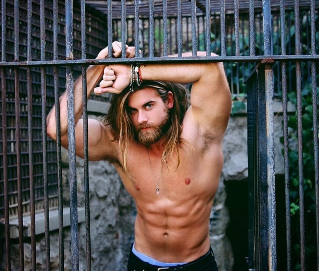 Brock O'Hurn leaning on a gate and flexing his upper body for a photoshoot