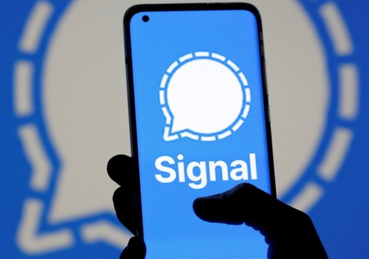 Right hand holding a smartphone displaying Signal icon amidst the same background
