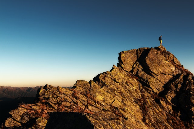 Male hiker with a backpack standing on the top edge of a huge rock formation on a cloudless day
