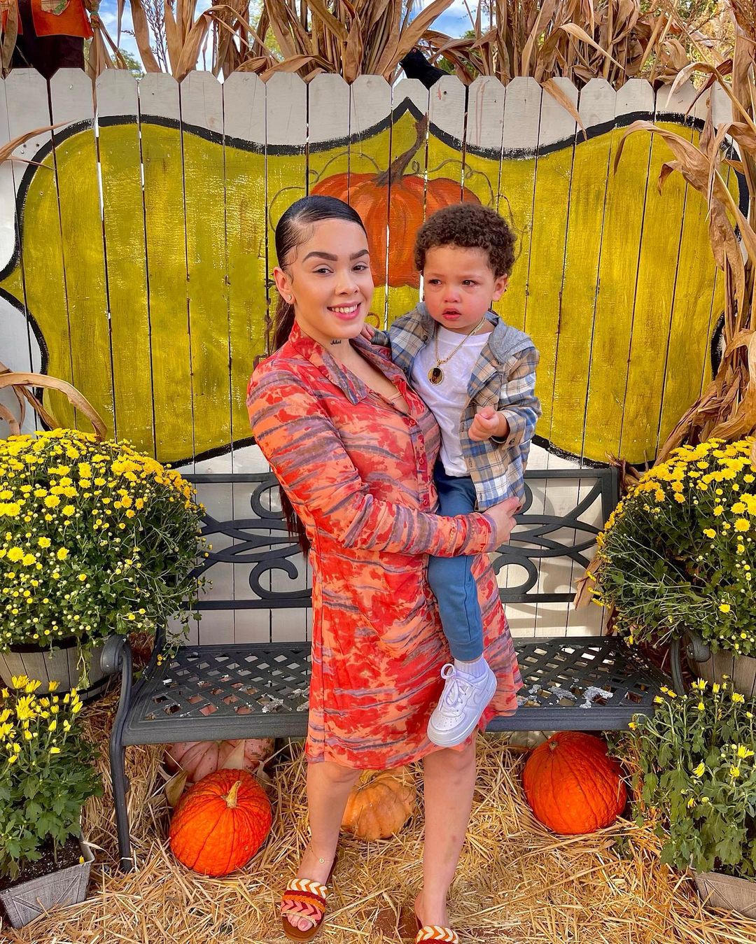 Jenesis Sanchez in orange dress carries a teary-eyed Gekyume Onfroy in an outdoor Halloween-themed photo booth