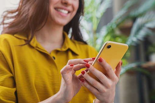 A woman who's wearing yellow top and has red nail polish is holding her yellow phone