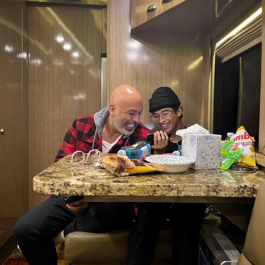 Jo Koy and Joseph Herbert Jr. share a laugh together while watching on a smartphone inside a tour bus