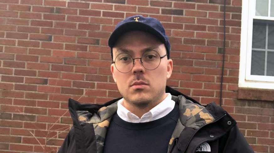 Anthony Fantano wearing baseball cap and round-rimmed glasses