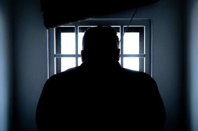 Back view of male prisoner looking outside through grilled cell window