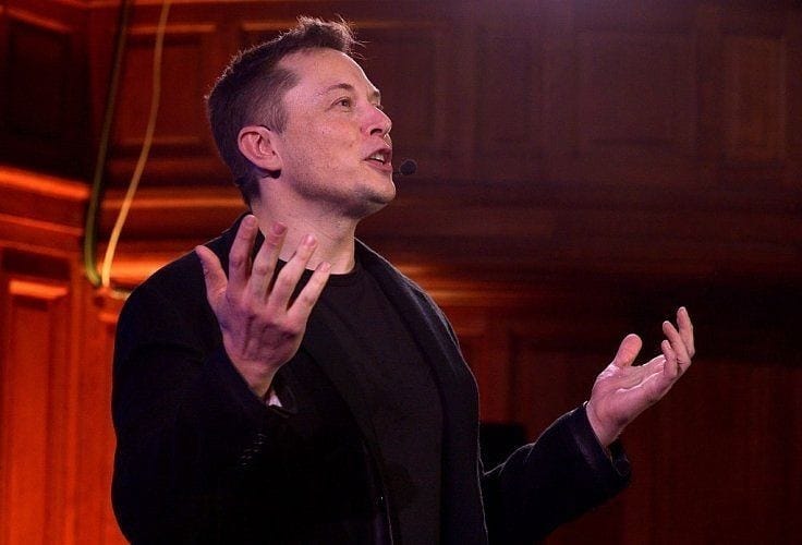 Tesla Motors CEO Elon Musk in black T-shirt and black blazer gesturing while giving a talk