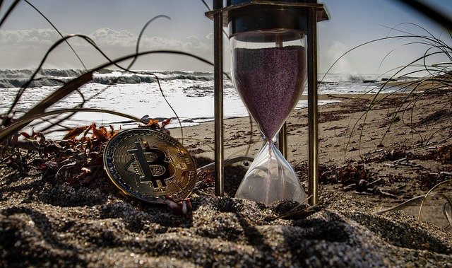 A Bitcoin beside an hourglass on the sand at the beach