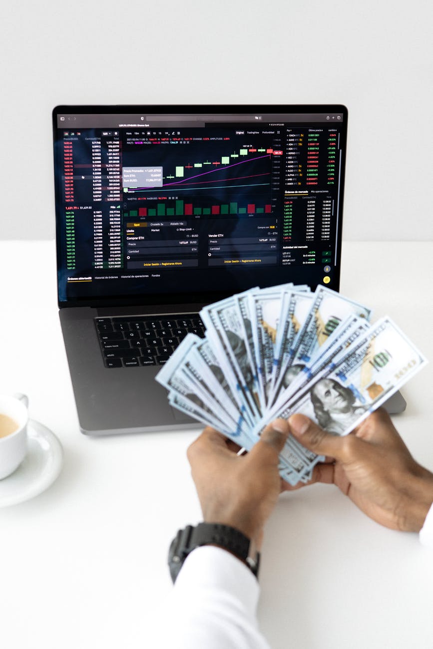 A man holding money with his cup of tea and black laptop showing stock rate analysis
