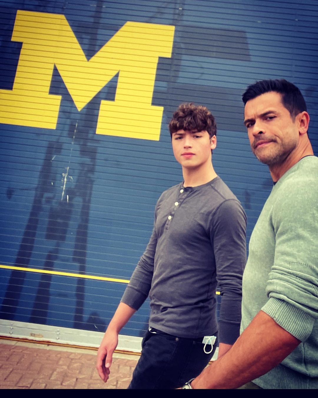 Joaquin Antonio Consuelo and Mark Consuelos walk past University of Michigan's yellow Block 'M' logo