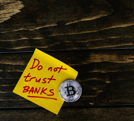 A silver Bitcoin on top of small yellow piece of paper, with the words ‘Do not trust banks’