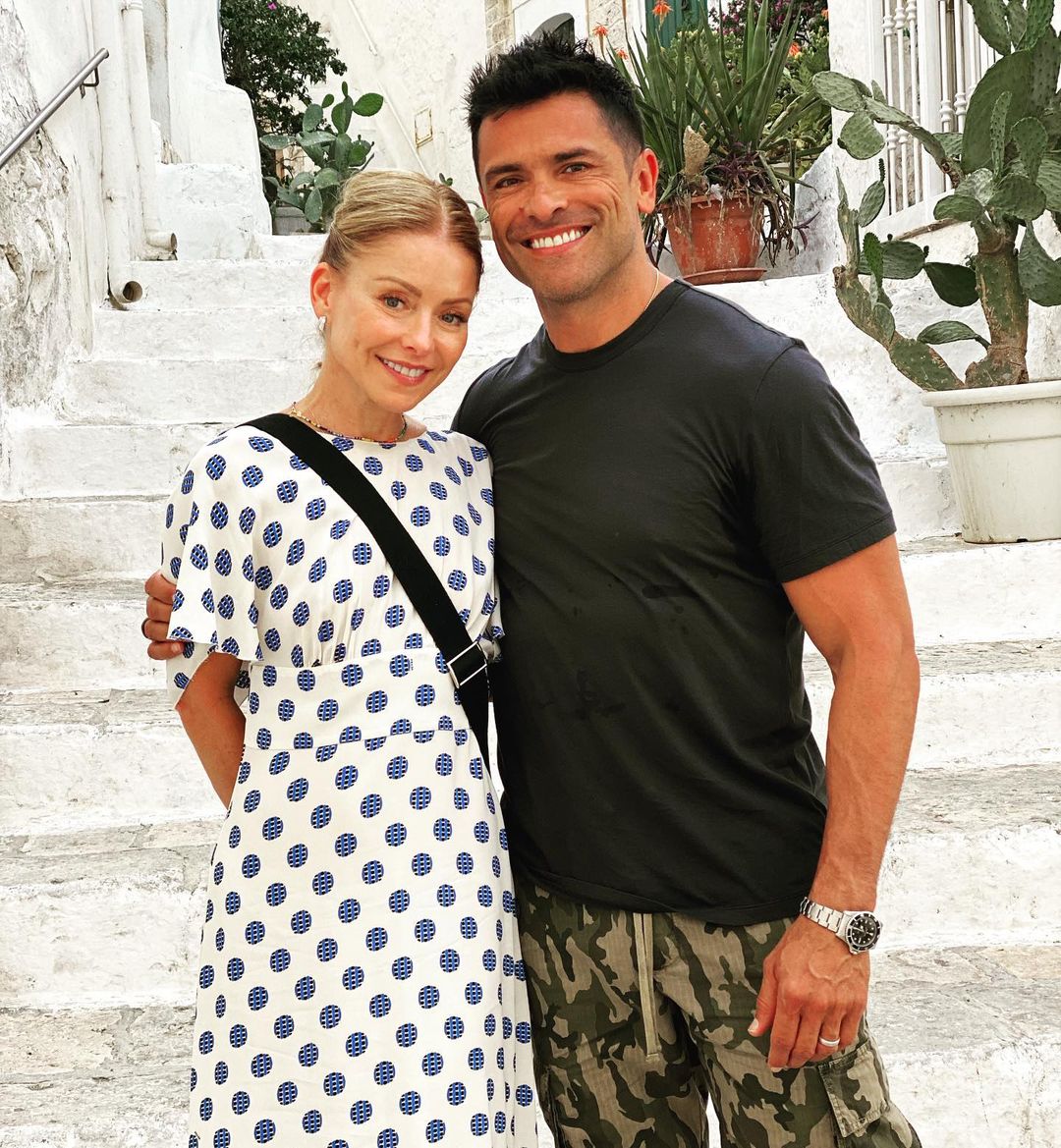 Kelly Ripa and Mark Consuelos posing close together at the bottom of a white painted stone staircase
