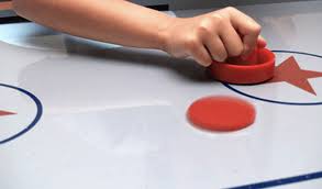 A hand holding a paddle strikes a puck on an air hockey table