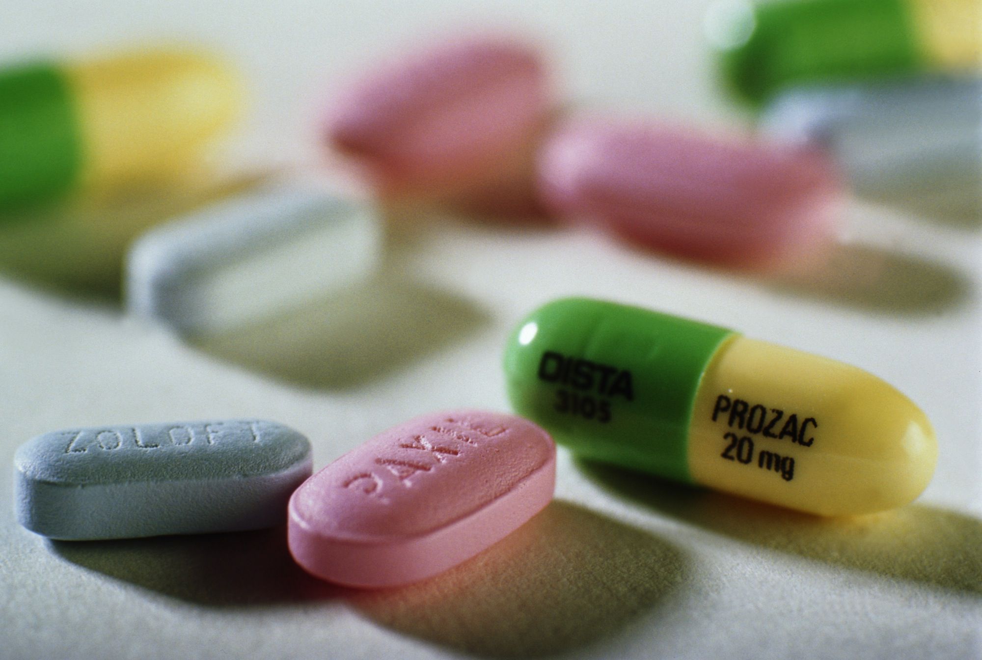 Yellow and green Prozac capsule with pink, blue, and white tablets all around on a white surface