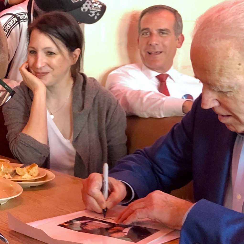 Elisa Pugliese rests her head on the palm of her hand with Eric Garcetti behind her as she shares a seat with Joe Biden