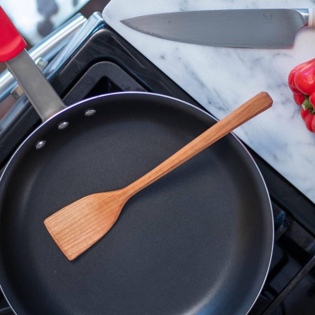Wooden spatula rests on an empty non-stick frying pan on top of a cooking range