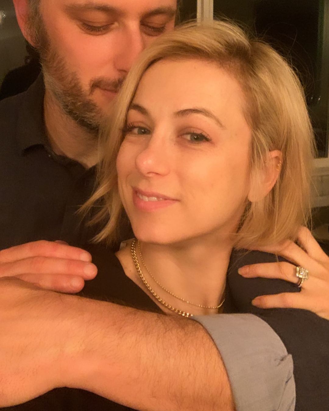 Iliza Shlesinger, wearing an emerald cut diamond engagement ring, gets embraced by Noah Galuten from the back