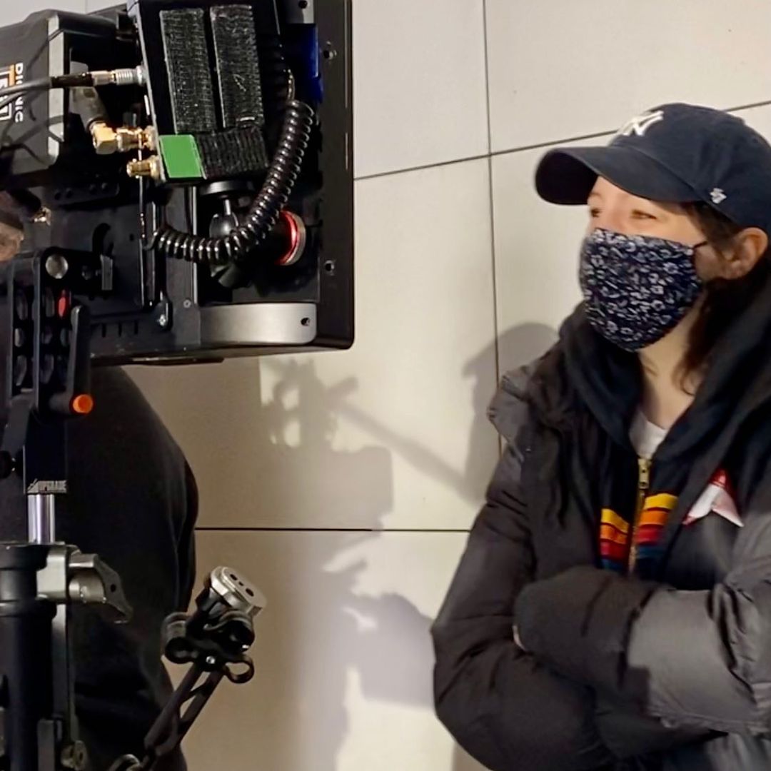 Elisa Pugliese in navy blue New York Yankees cap, thickened down jacket and cloth facemask looks at the film monitor