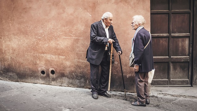 Old man holding two canes and old woman out in a pavement