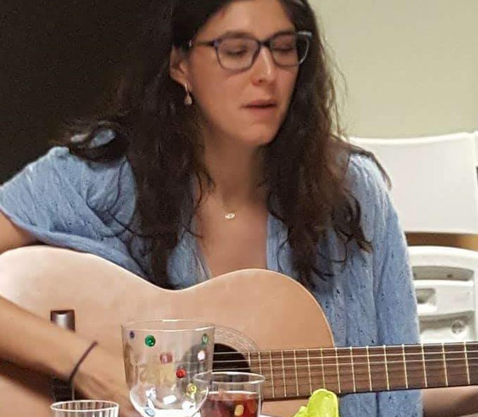 Emily Beth Stern wears eyeglasses as she plays the guitar
