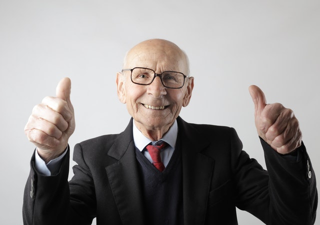 Smiling old man in formal suit and black-rimmed eye glasses making a thumbs up sign