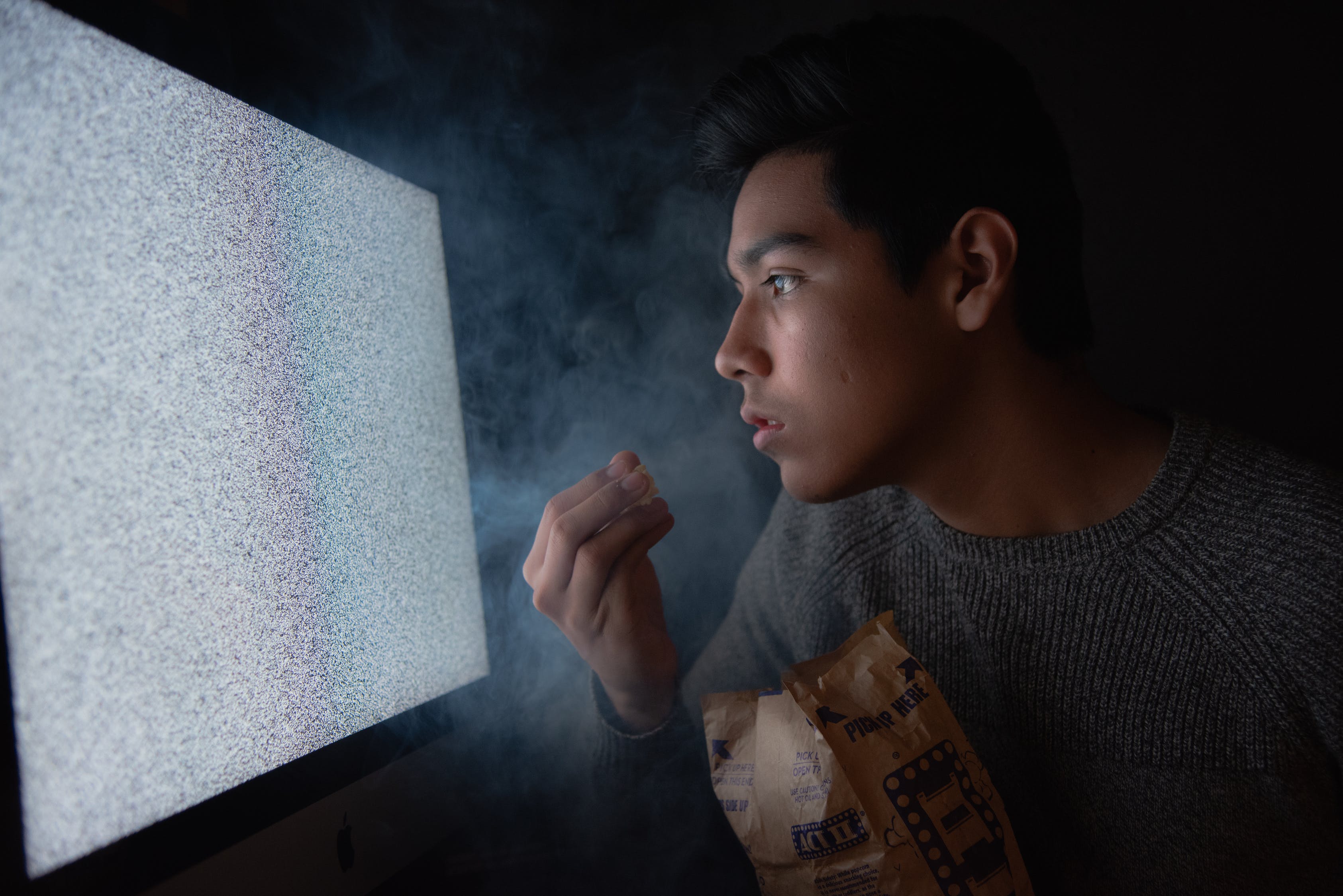 A man watching so close to the TV while eating a popcorn