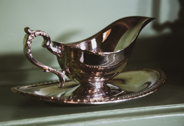 An antique silver sauce boat with intricate handle on a silver platter