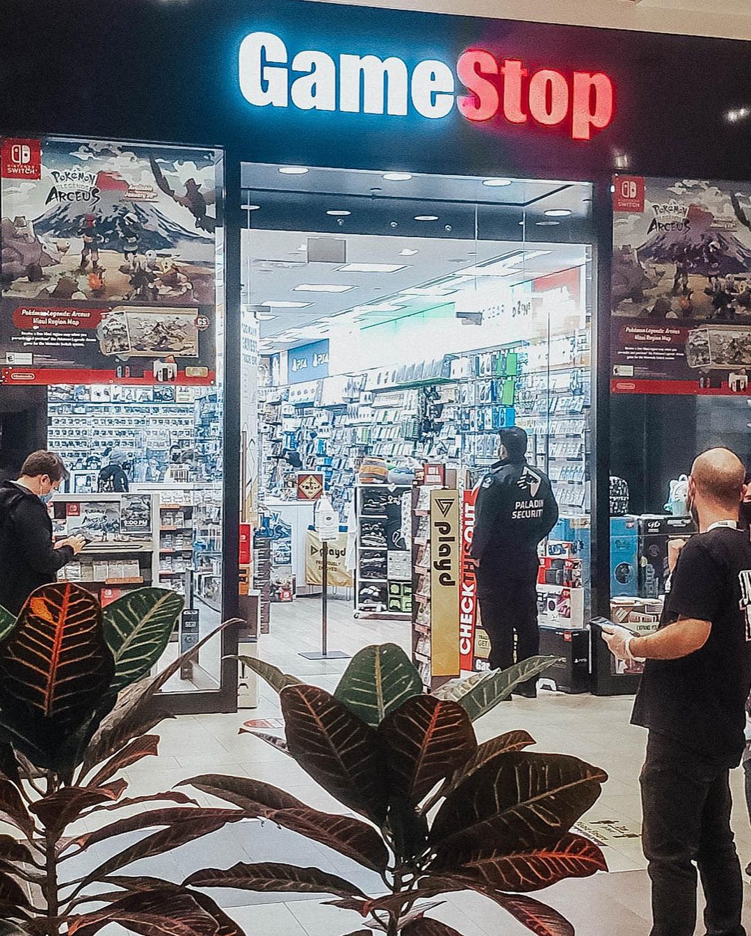 Three adult men outside a GameStop store in Canada, with one at the entrance looking inside