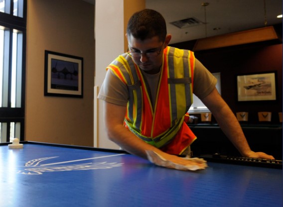 A man wearing a safety vest wipes the surface of the air hockey table