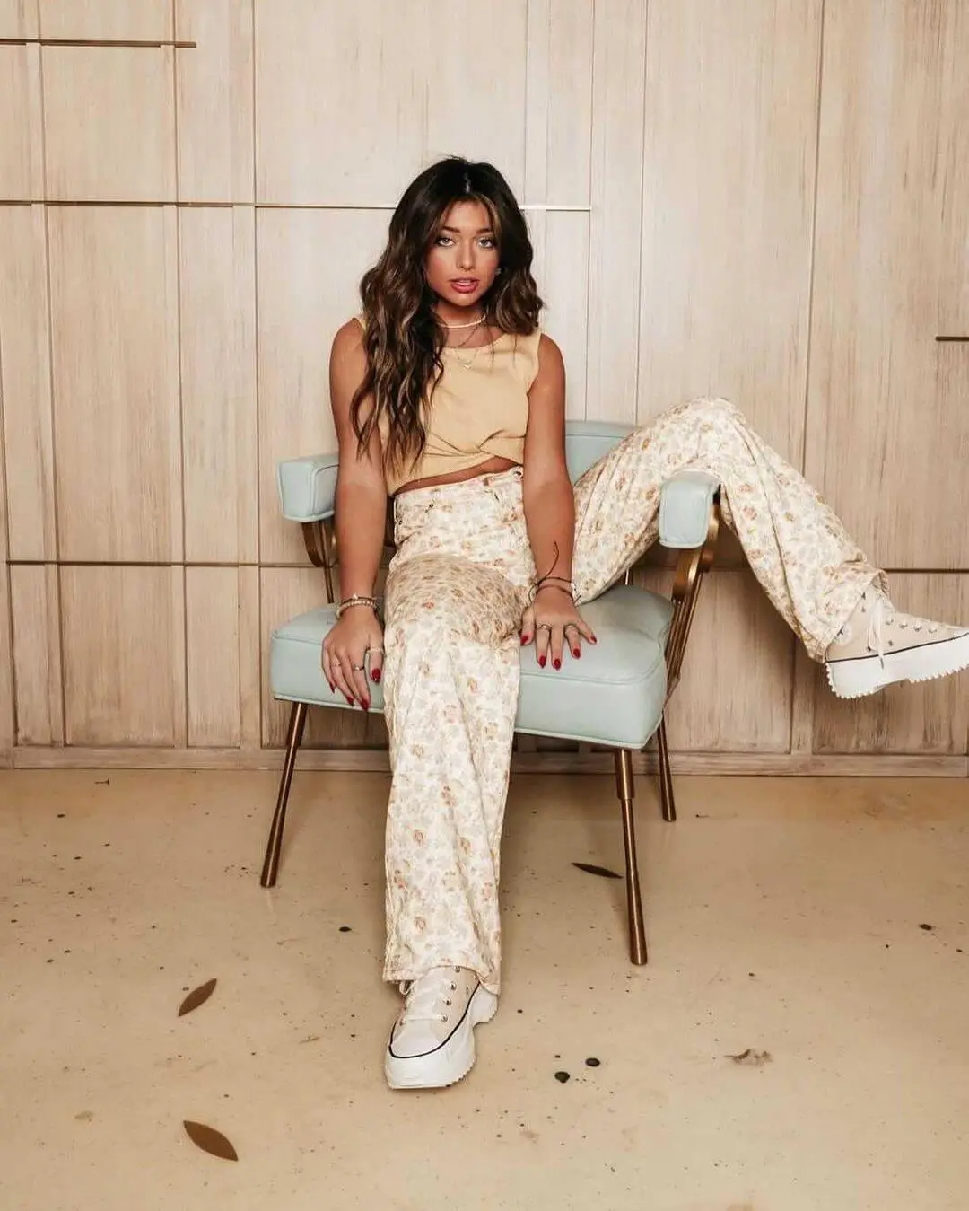 Tabitha Swatish wearing a cream crop top, light cream high-waist pants, and white sneakers while sitting like a boss on a gray chair