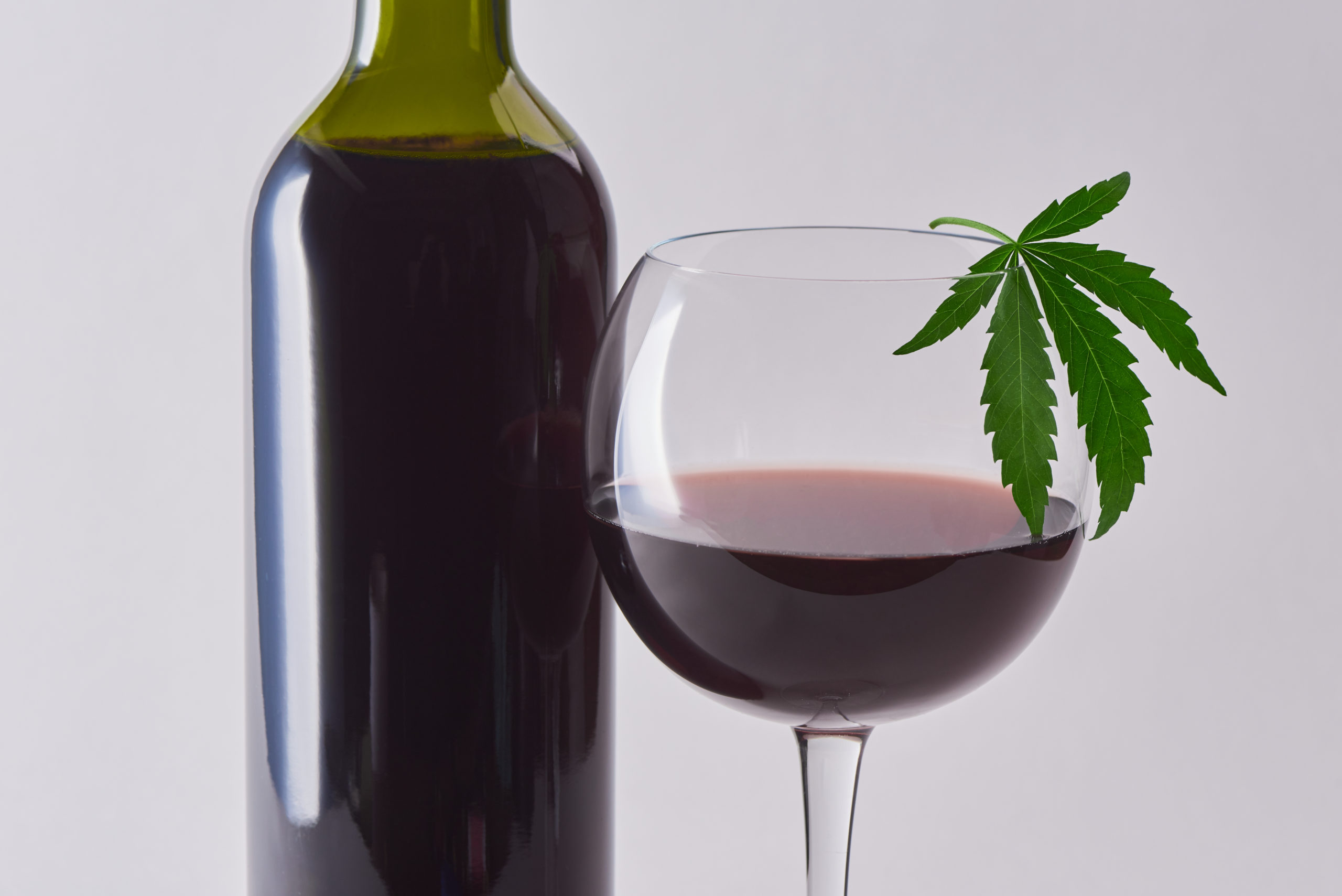 A filled bottle of wine and a half-filled glass of wine having a cannabis leaf at its tip