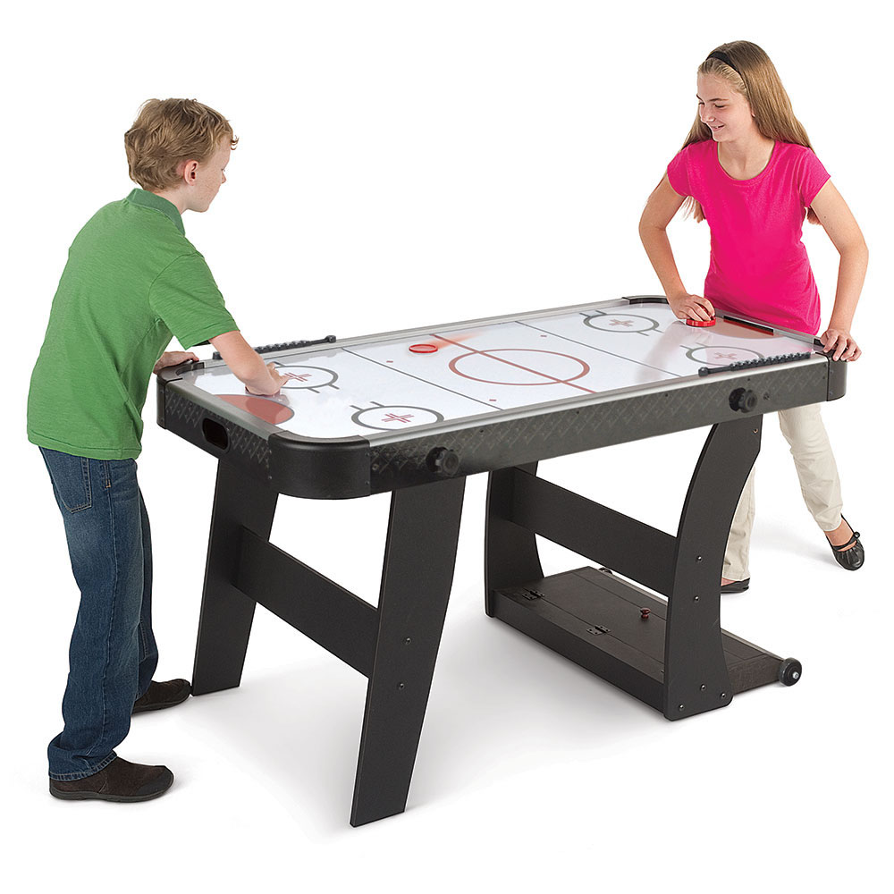 A young boy and a young girl playing air hockey on a foldable air hockey table