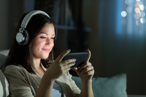 A relaxed woman watching on her phone with her headphones on inside the comfort of her home
