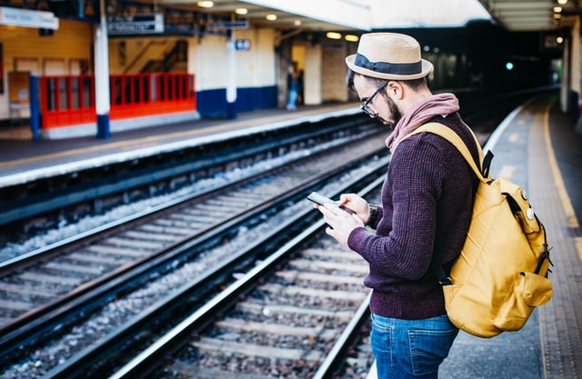 Male fashion blogger checks his blog on his smartphone while waiting for the train