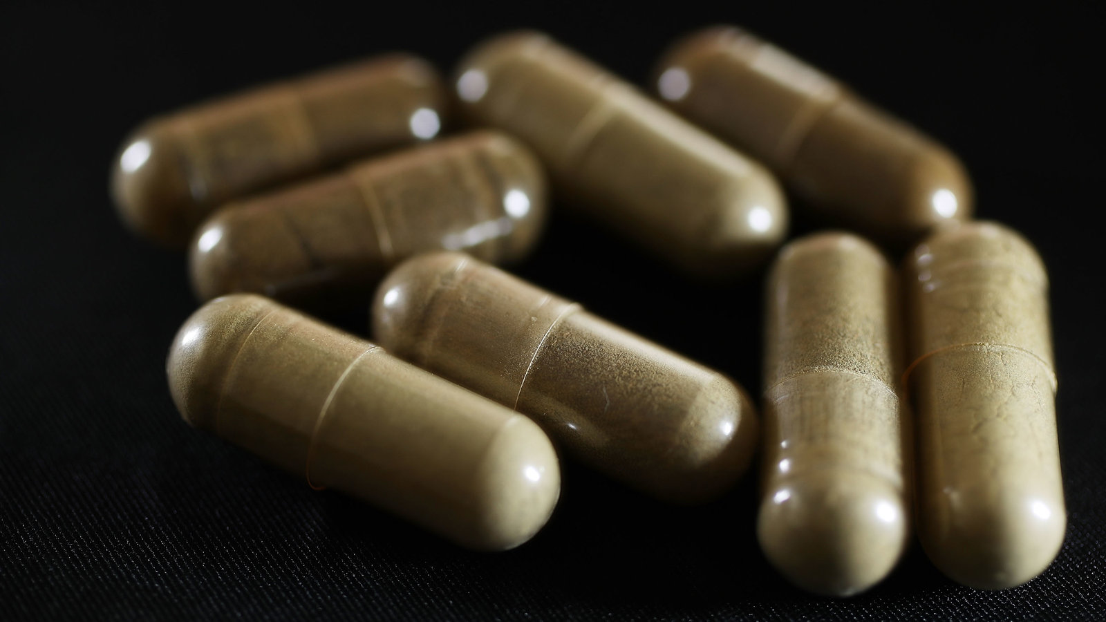 Eight pills of CBD Kratom in a black background