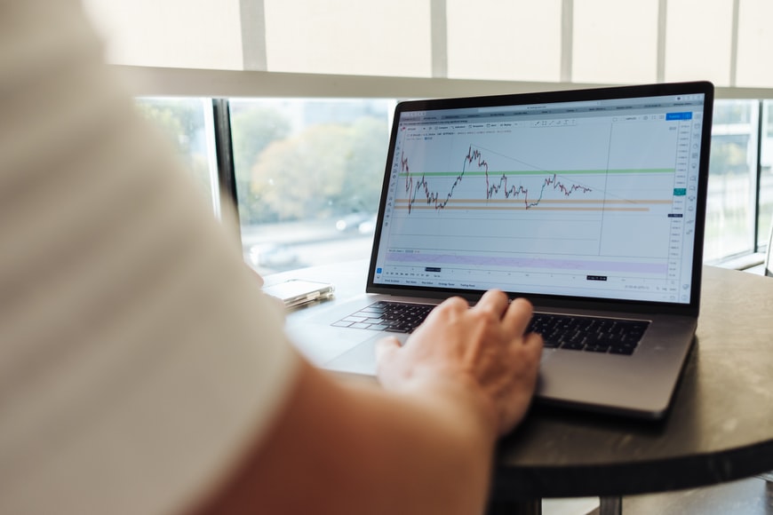 One hand typing on a laptop with trading charts