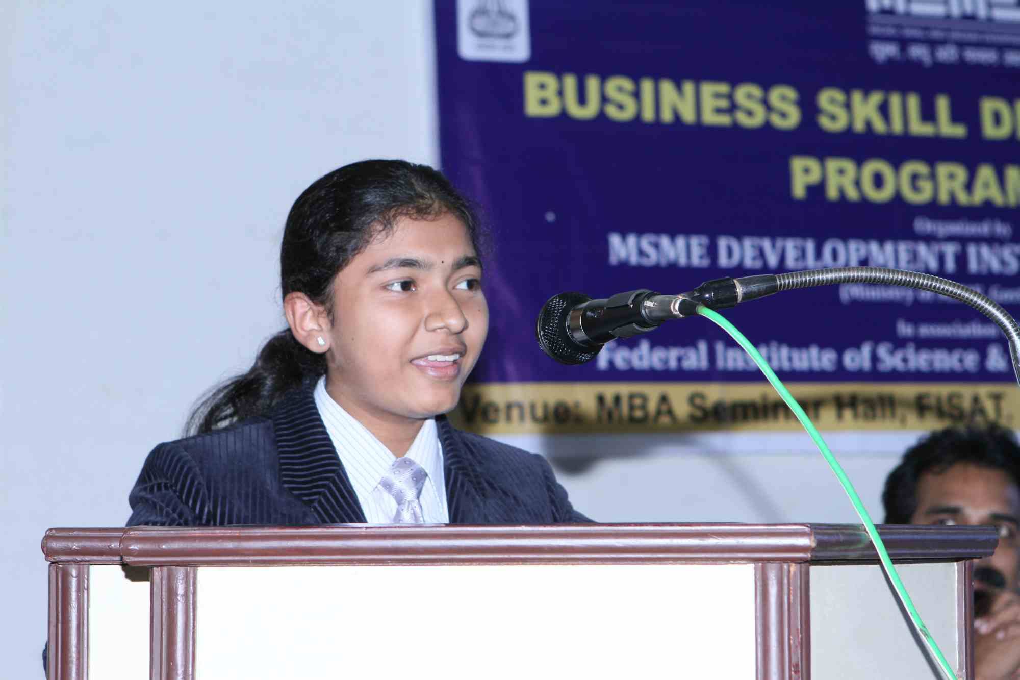 Sreelakshmi Suresh in an American business suit at the podium at FISAT in Kochi