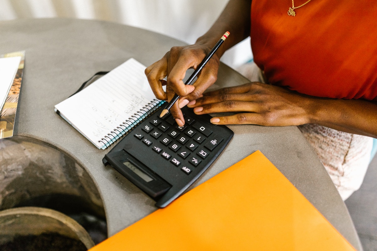 A girl holding a pencil while using the calculator and a notebook beside it