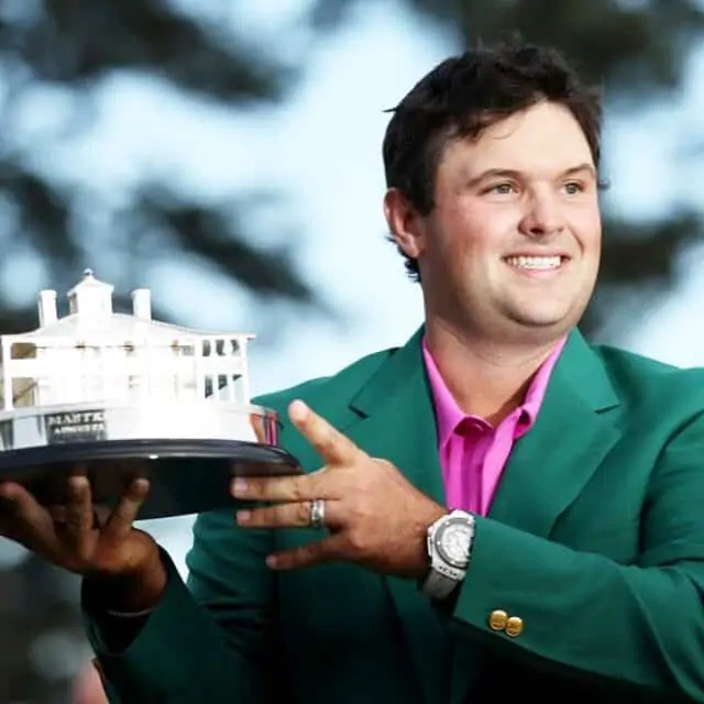 Patrick Reed, Holding A Model Of A Building In His Hands While Wearing A Green Sports Coat