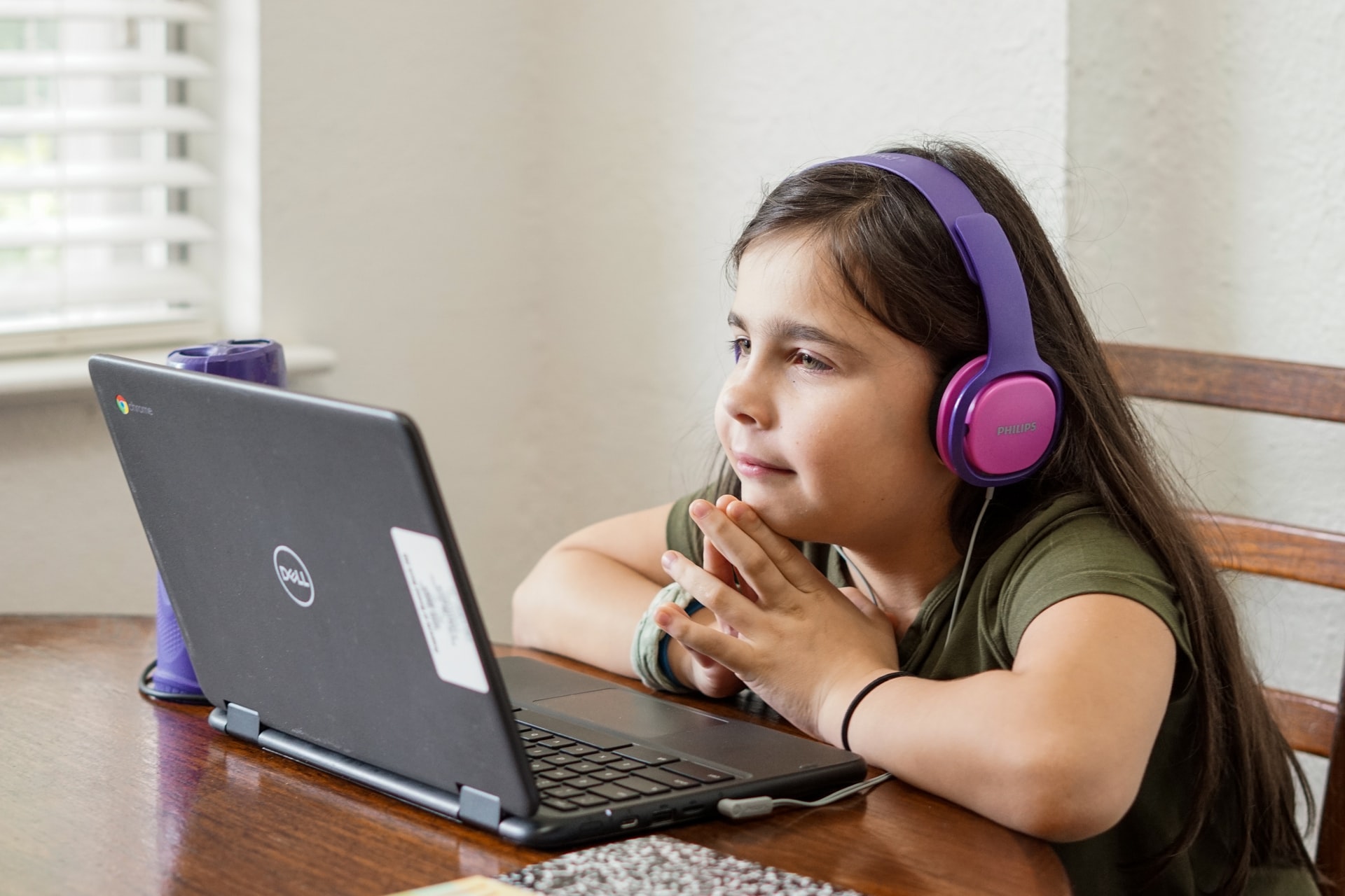 A female elementary student with a Philips headset and a Dell laptop attends an online class