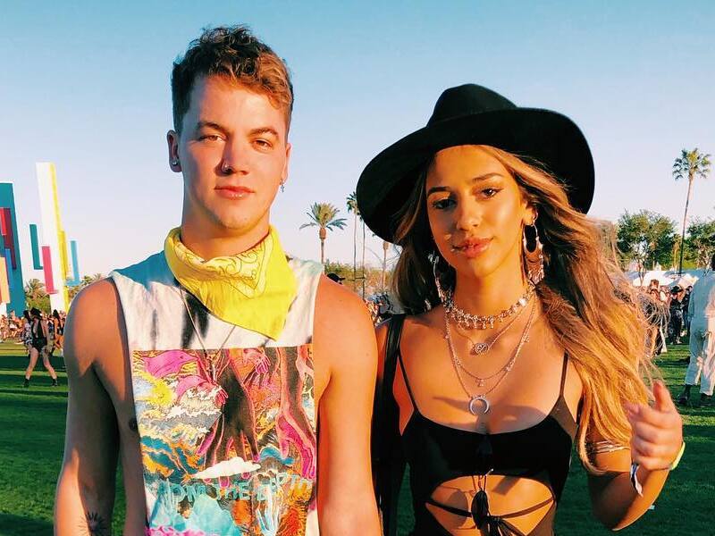 Carolina Samani wearing a black swimsuit, black hat, and silver necklaces, and Taylor Caniff wearing a white tank top and yellow bandana on his neck