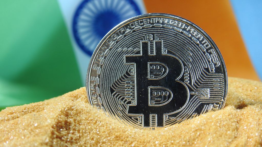 Silver bitcoin token in a sand and India flag behind it