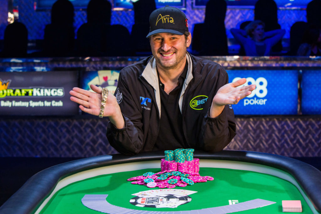 Smiling Phil Hellmuth holding a bracelet with poker chips and cards on the table