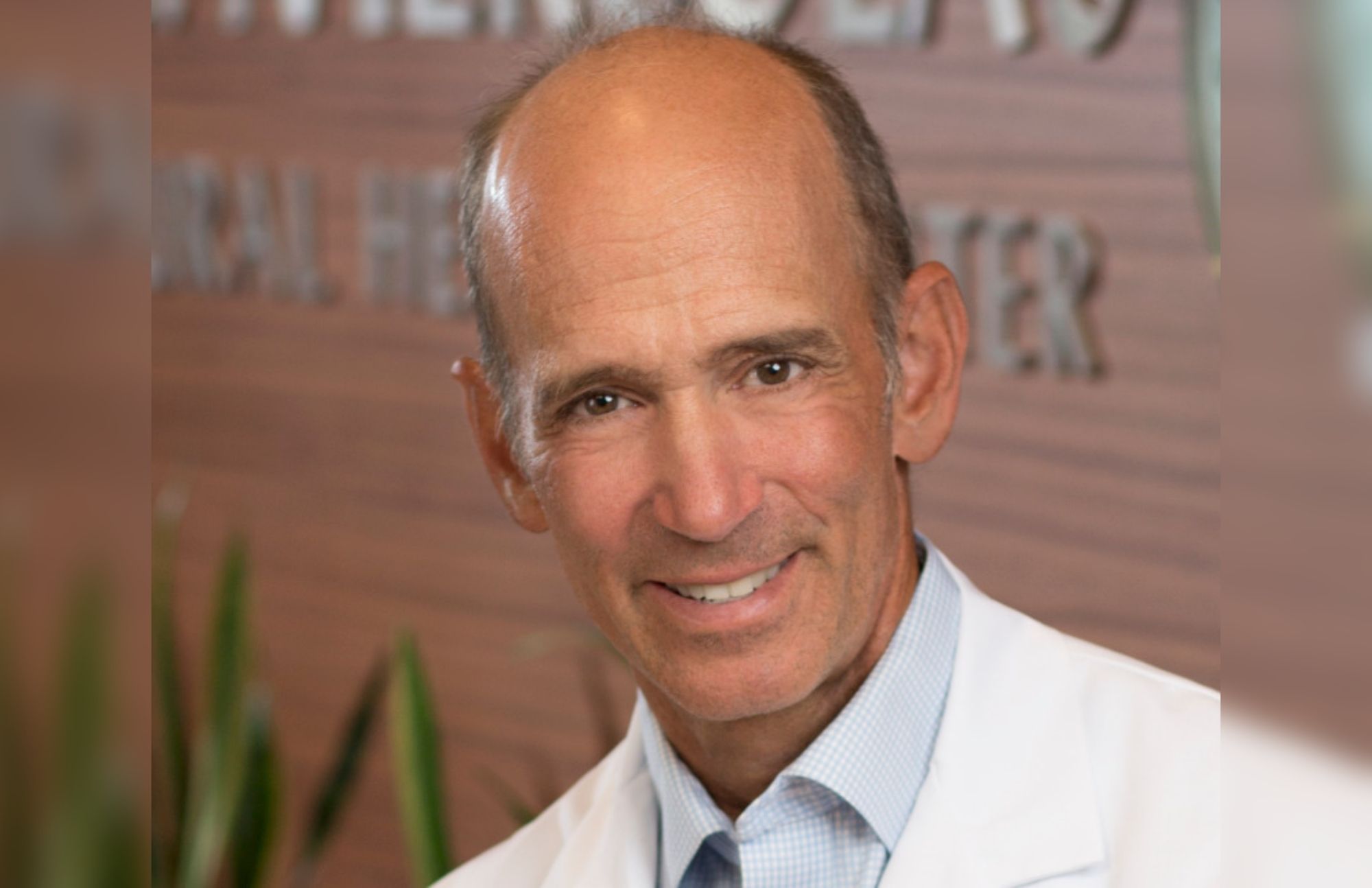 Dr. Joseph Mercola wearing a laboratory gown and is smiling at the camera