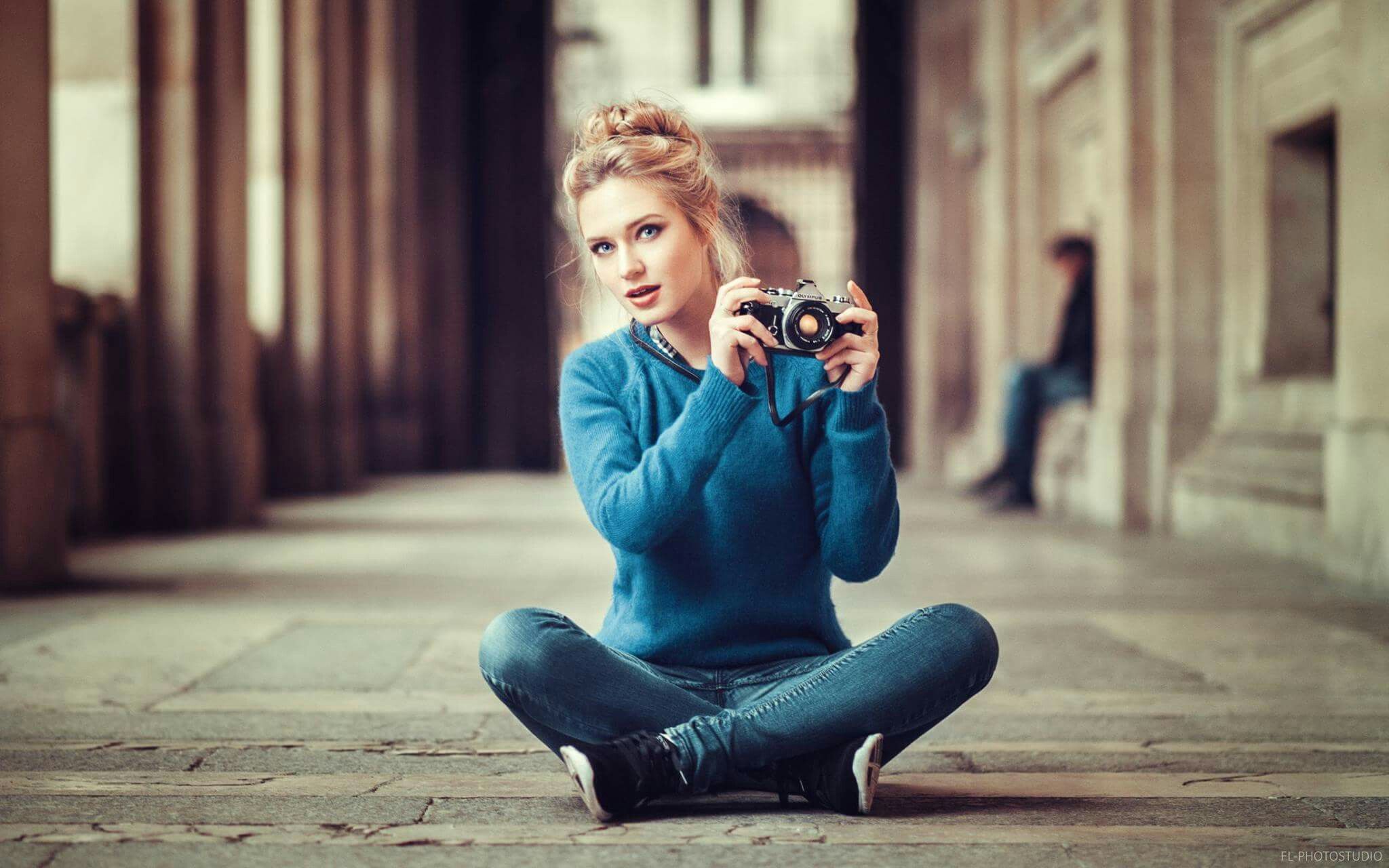 Eva Mikulski wearing blue long sleeves and denim pants while holding a camera