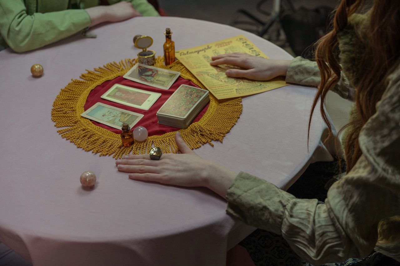 Two Persons Sitting In Front Of A Table With Tarot Cards And Small Crystal Balls